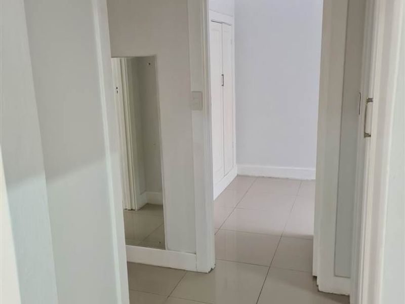 A clean, neutral hallway featuring tiled flooring and access to adjacent rooms, providing a bright and functional transition space within the apartment.