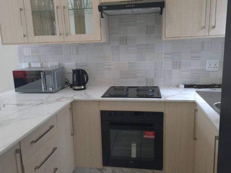 A well-maintained kitchen featuring light wood-finish cabinetry, marble-look countertops, a built-in oven, electric hob, and a modern tiled backsplash.
