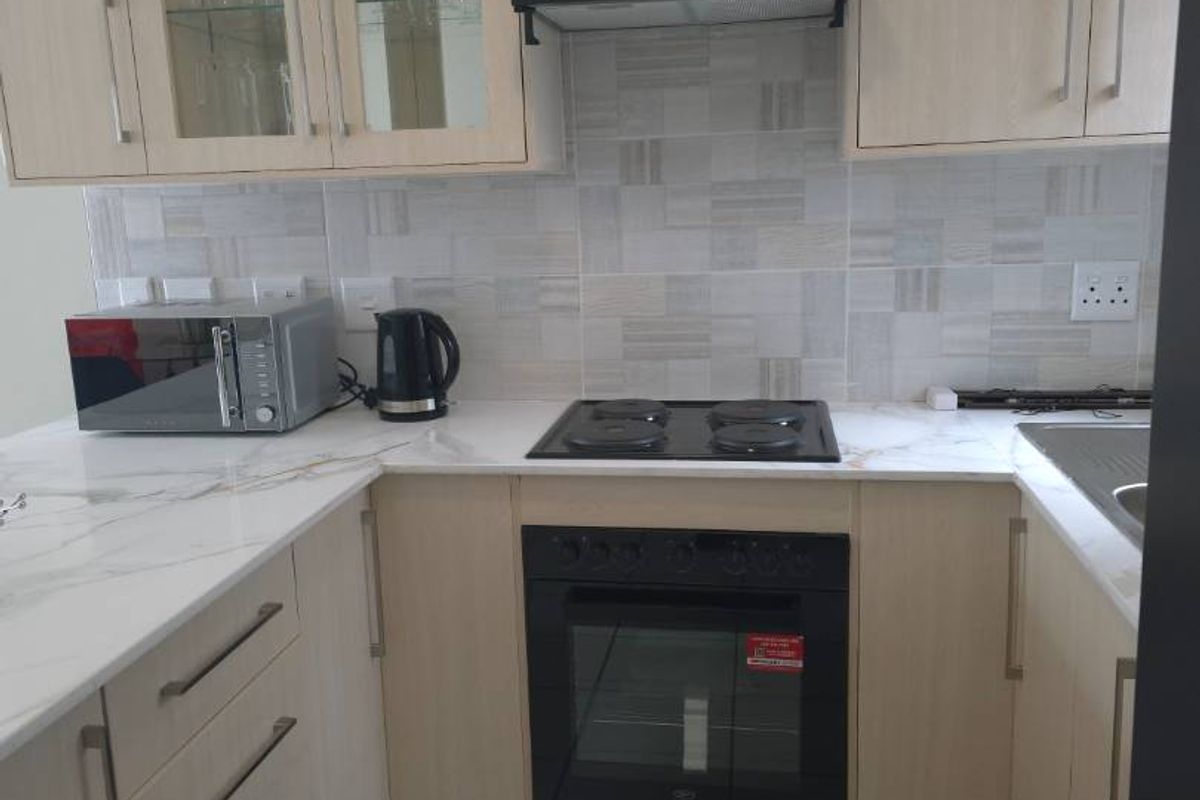 A well-maintained kitchen featuring light wood-finish cabinetry, marble-look countertops, a built-in oven, electric hob, and a modern tiled backsplash.