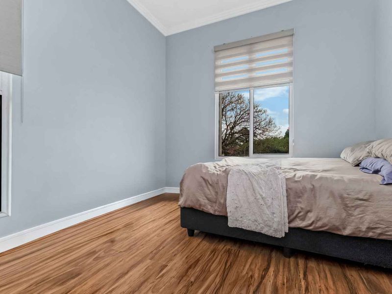A bright bedroom featuring laminate flooring, neutral wall tones, and large windows with fitted roller blinds, offering a clean and well-maintained living space.