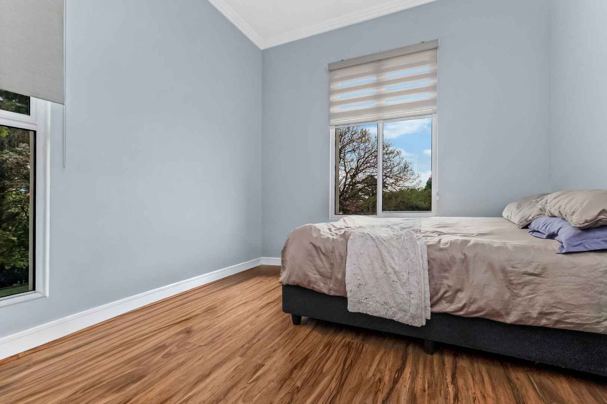 A bright bedroom featuring laminate flooring, neutral wall tones, and large windows with fitted roller blinds, offering a clean and well-maintained living space.