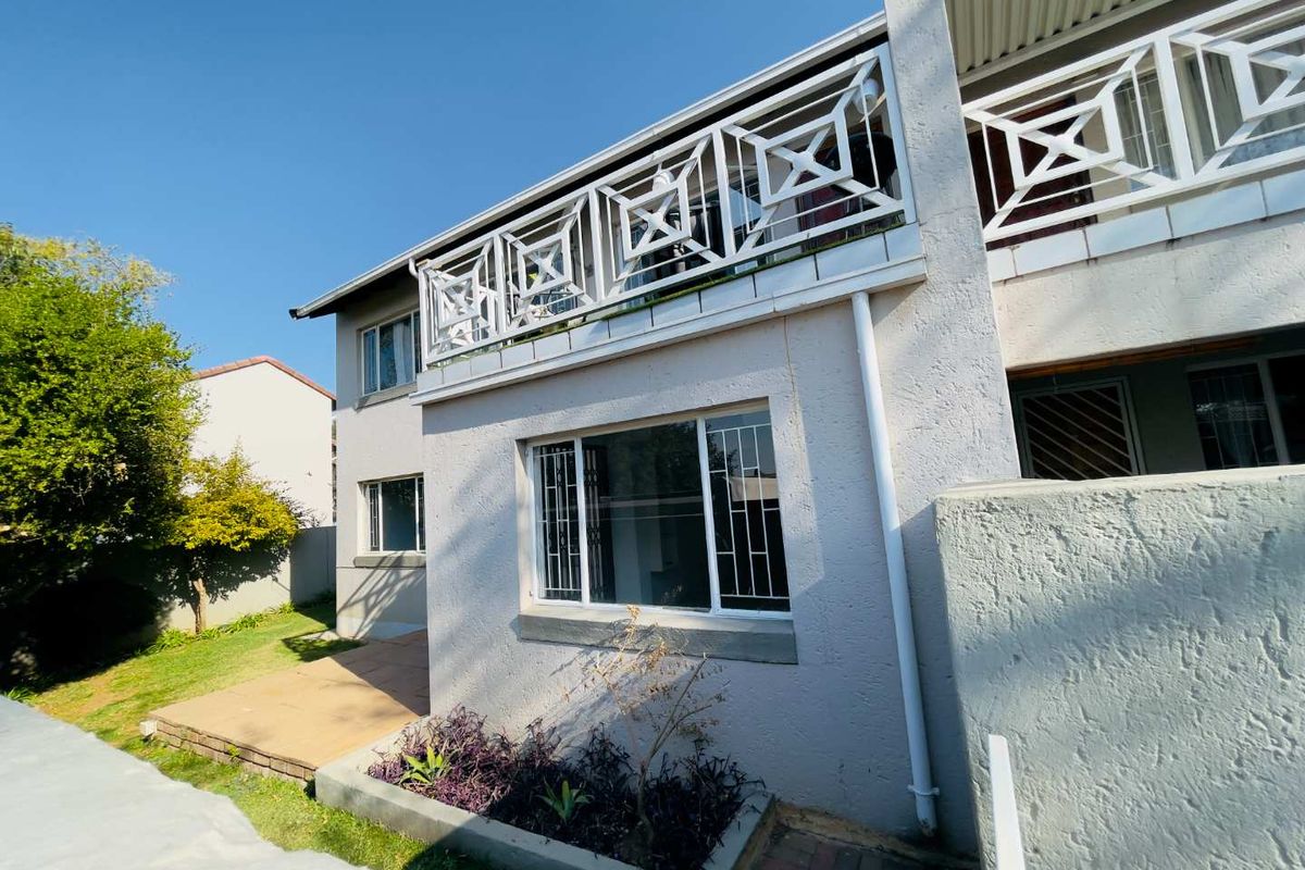 Rear view of the apartment building featuring a balcony with metal balustrades, security bars on windows, a paved patio area, and a raised garden bed.