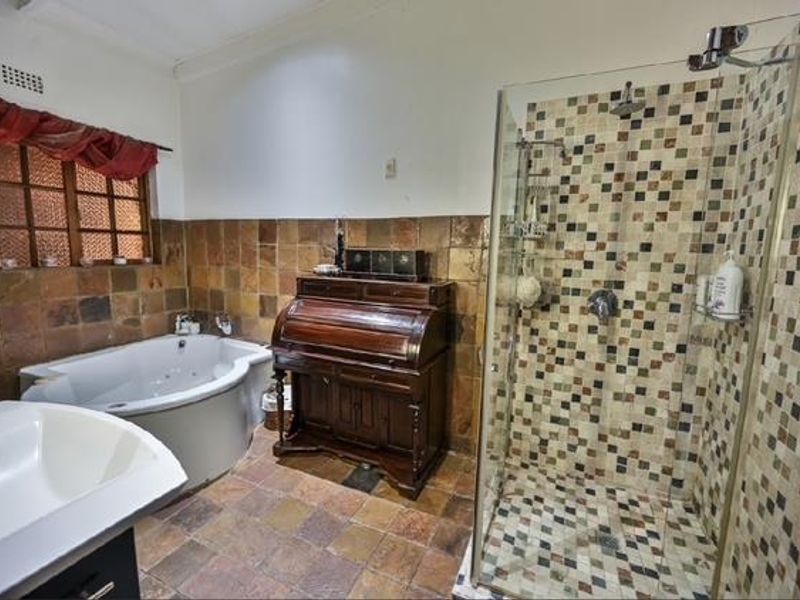 A bathroom featuring a corner bathtub, a walk-in shower with mosaic tiling, and a vanity basin, finished with earthy-toned wall and floor tiles.