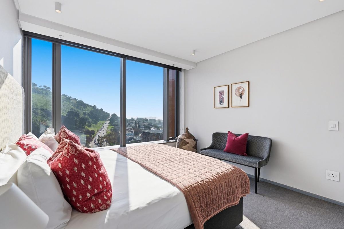 A modern bedroom featuring floor-to-ceiling windows with expansive city and mountain views, neutral finishes, and recessed lighting.