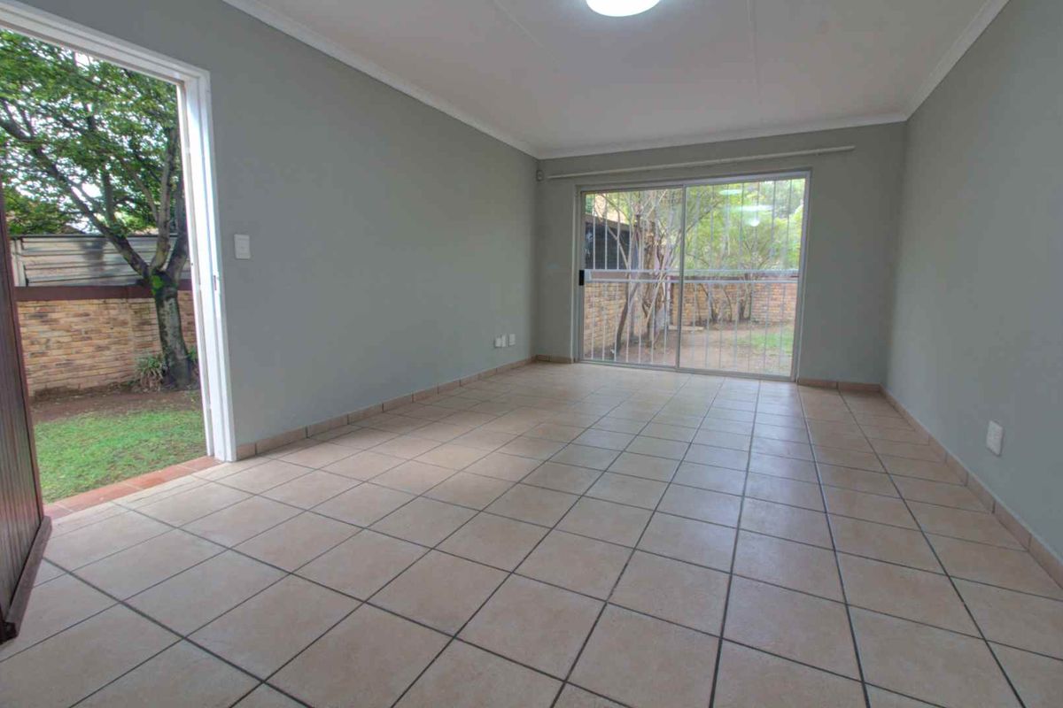 A bright, empty living room featuring neutral tiled flooring and large sliding glass doors that provide direct access to the rear garden area.