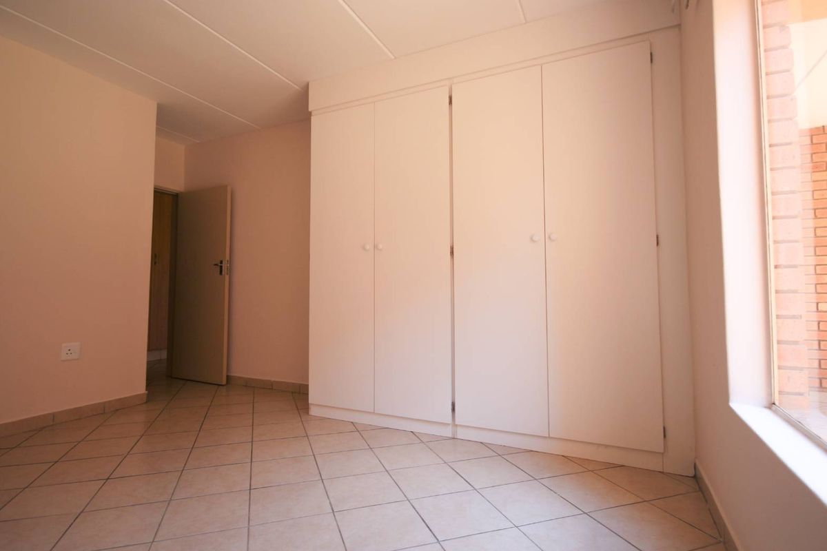 A bright, empty bedroom featuring neutral tiled flooring and ample built-in cupboard storage space.
