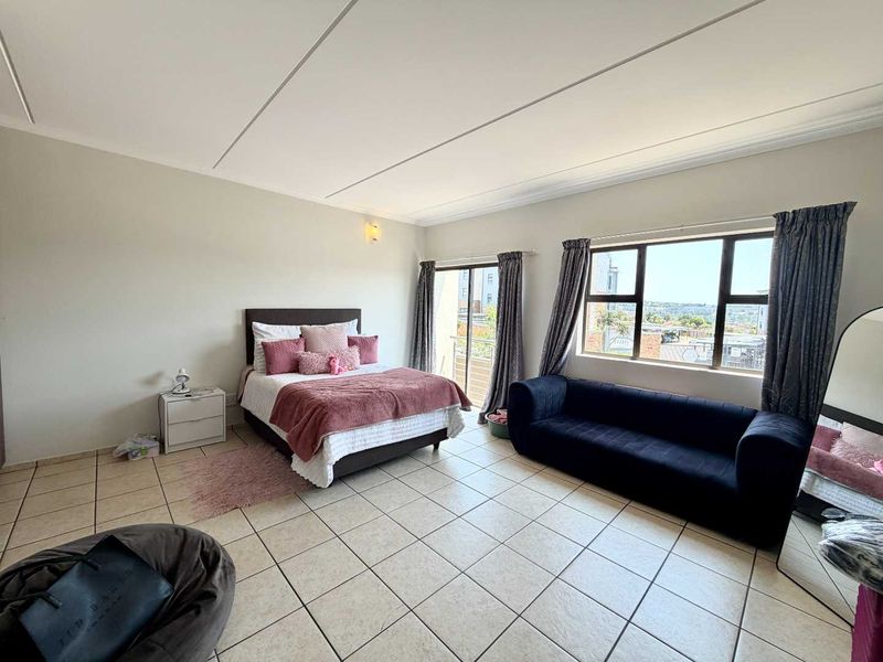 Spacious bedroom featuring tiled flooring, large windows for natural light, and a sliding door providing access to an outdoor area.