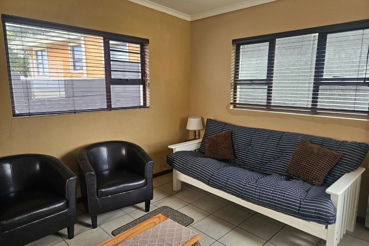 A living room featuring tiled flooring and horizontal window blinds, showing signs of wear on the wall surfaces.