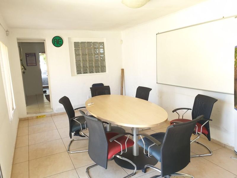 A functional office meeting room featuring tiled flooring, a wall-mounted whiteboard, and a glass block window providing natural light.
