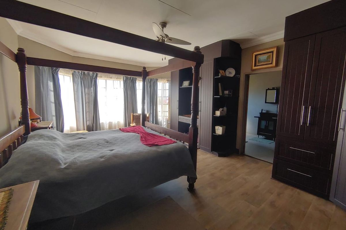 Spacious bedroom featuring laminate flooring, built-in cupboards, a ceiling fan, and a bay window, with an adjoining en-suite bathroom visible.