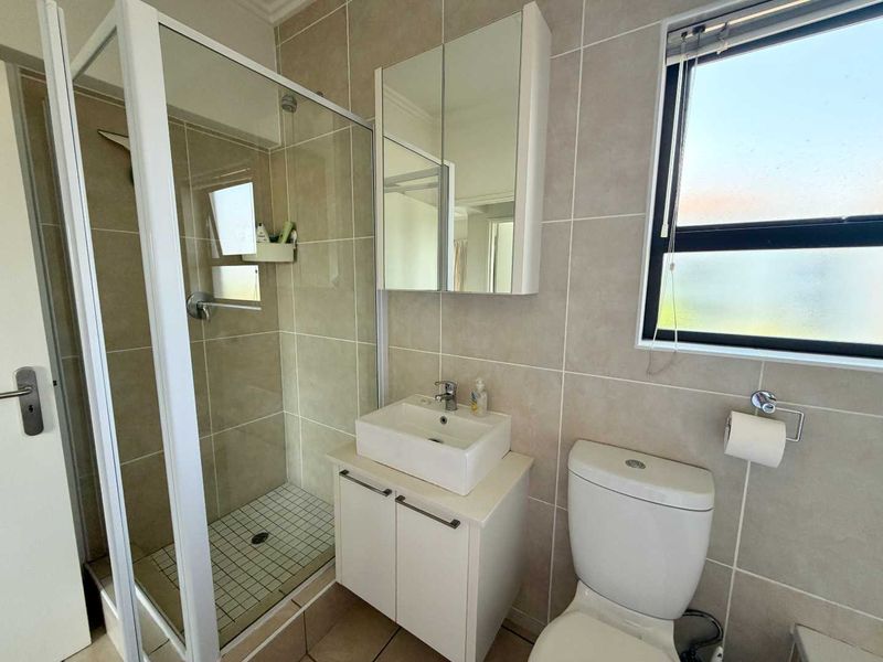 A clean, modern bathroom featuring a glass shower enclosure, vanity with basin, mirrored cabinet, and tiled finishes throughout.