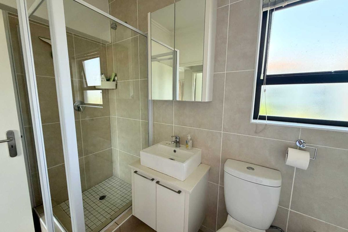 A clean, modern bathroom featuring a glass shower enclosure, vanity with basin, mirrored cabinet, and tiled finishes throughout.
