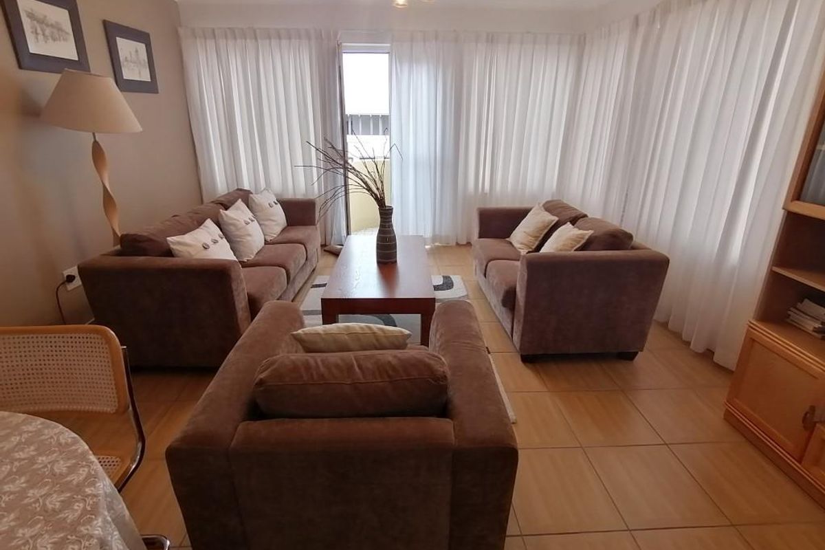 A comfortable living room featuring tiled flooring, neutral wall tones, and a sliding glass door providing access to an outdoor balcony area.