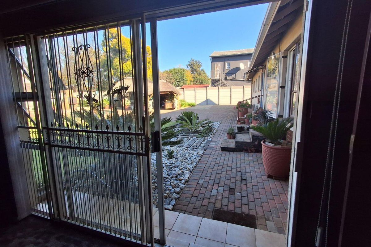 View from an interior space looking out onto a paved rear courtyard with landscaped garden beds and a security gate.