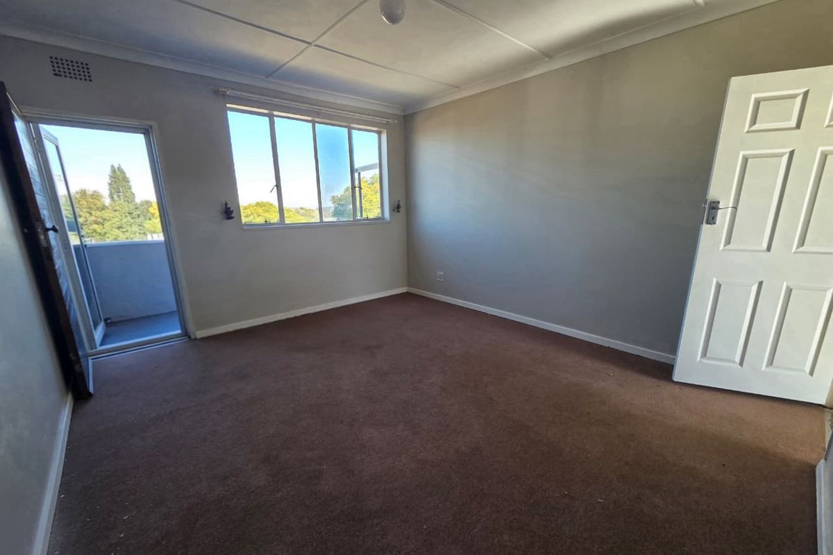 An empty bedroom featuring carpet flooring, large windows providing natural light, and direct access to a private balcony.