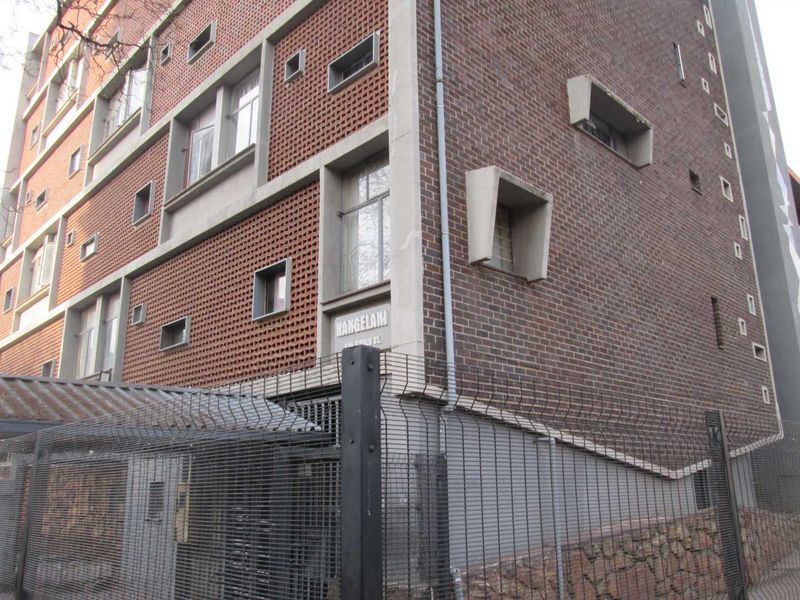 Exterior view of the Kangelani apartment building, featuring a distinctive brick facade with concrete architectural detailing and secure perimeter fencing.