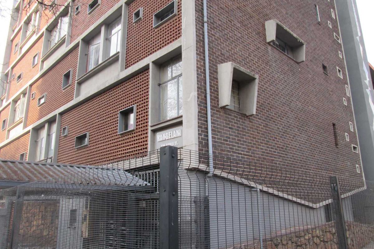 Exterior view of the Kangelani apartment building, featuring a distinctive brick facade with concrete architectural detailing and secure perimeter fencing.