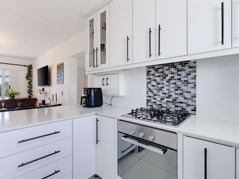 Modern kitchen featuring white cabinetry, quartz countertops, a mosaic tile backsplash, and integrated stainless steel gas cooktop and oven.
