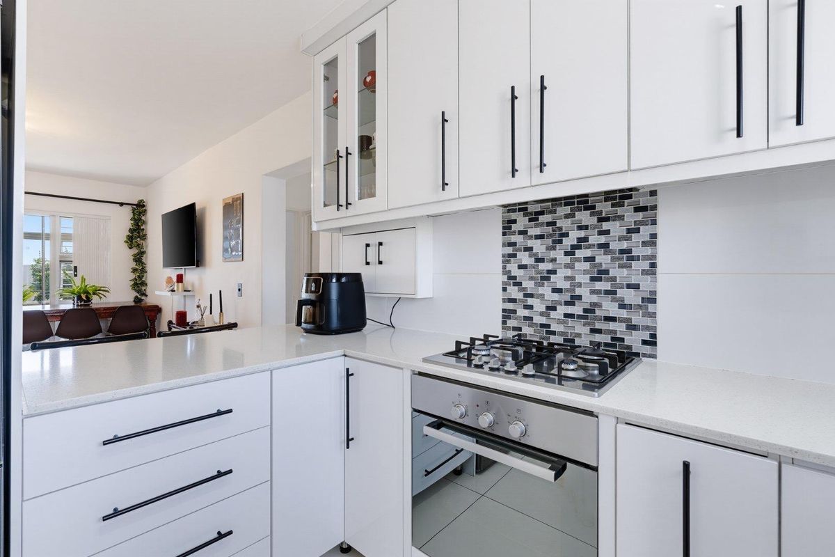 Modern kitchen featuring white cabinetry, quartz countertops, a mosaic tile backsplash, and integrated stainless steel gas cooktop and oven.