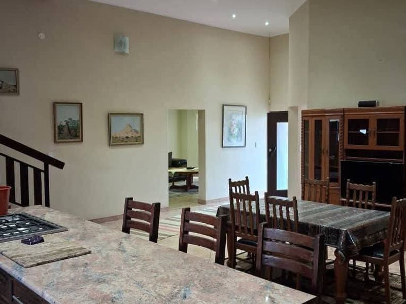 Spacious open-plan living and kitchen area featuring a large granite island, gas hob, recessed lighting, and exposed timber ceiling beams.