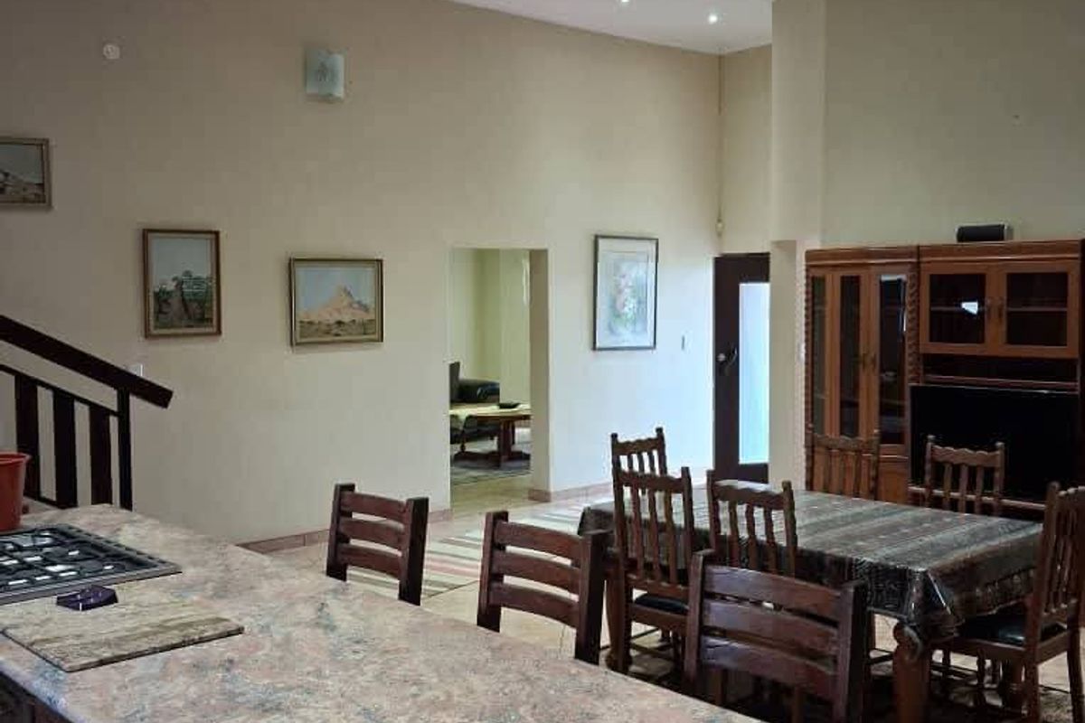 Spacious open-plan living and kitchen area featuring a large granite island, gas hob, recessed lighting, and exposed timber ceiling beams.