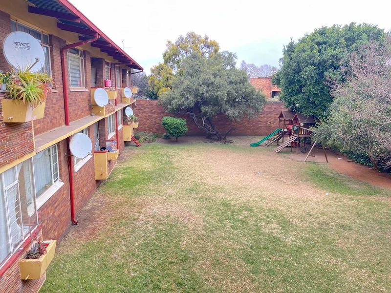 View of the rear communal garden area featuring a large lawn, mature trees, and the brick facade of the apartment building.