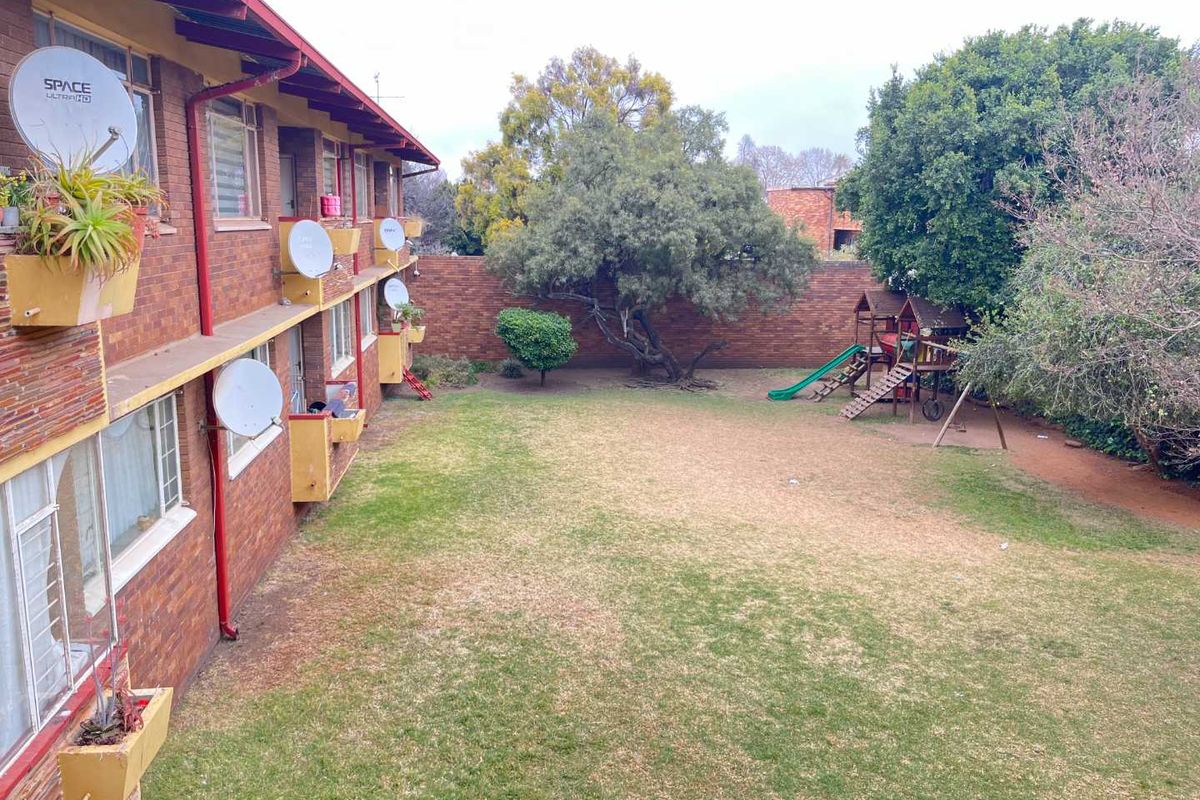 View of the rear communal garden area featuring a large lawn, mature trees, and the brick facade of the apartment building.