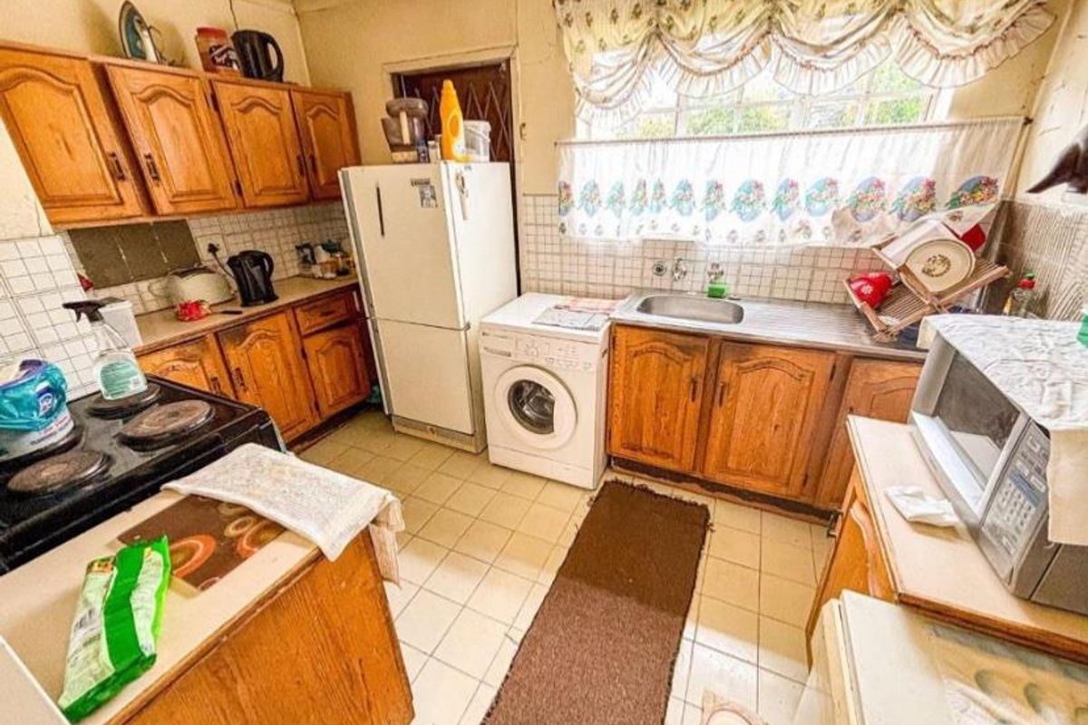 A dated kitchen featuring traditional timber cabinetry, tiled flooring, and a functional layout with integrated sink and appliance space.