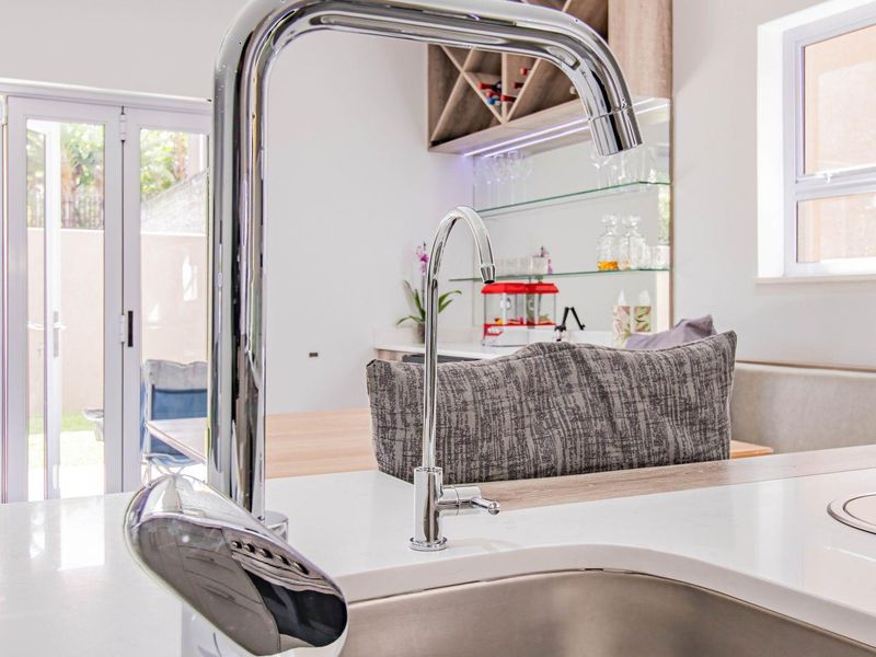 Modern kitchen featuring a sleek quartz countertop, stainless steel sink with chrome mixer tap, and integrated glass shelving with built-in wine storage.