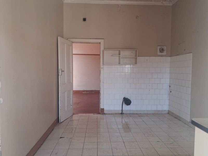 An empty, dated kitchen area featuring tiled flooring, a tiled splashback, and wall-mounted shelving, requiring renovation to modernize the space.