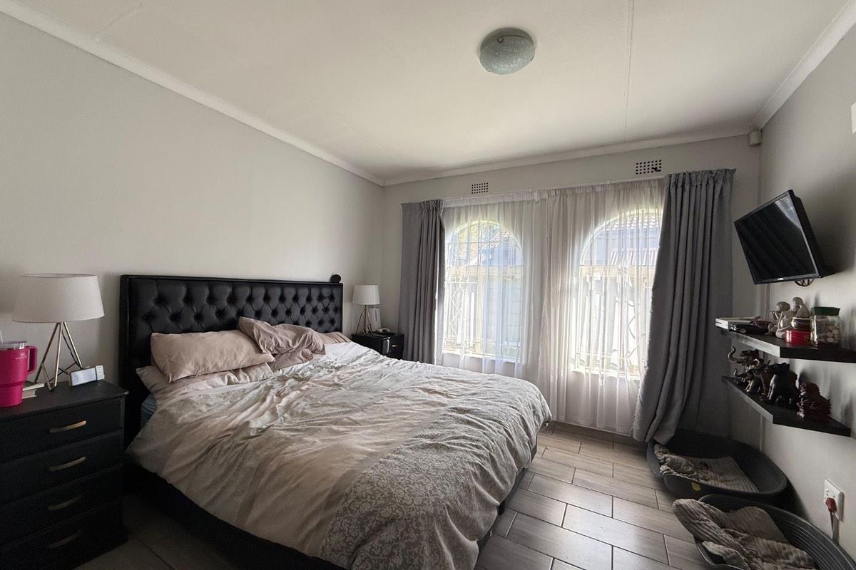 A well-lit bedroom featuring tiled flooring, arched windows with curtain treatments, and a central ceiling light fixture.
