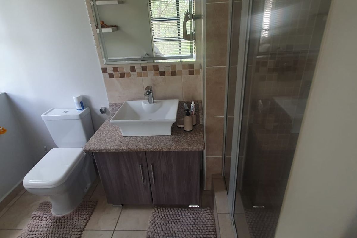 A functional bathroom featuring a vessel sink on a granite vanity, a glass shower enclosure, and neutral wall and floor tiling.
