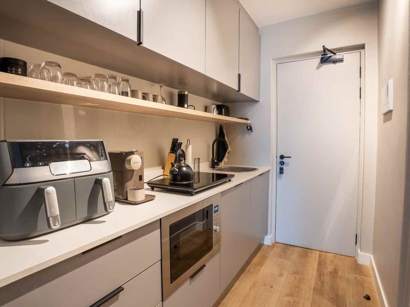 Modern compact kitchen featuring sleek grey cabinetry, stone countertops, integrated microwave, induction hob, and stylish timber shelving with wood-look laminate flooring.