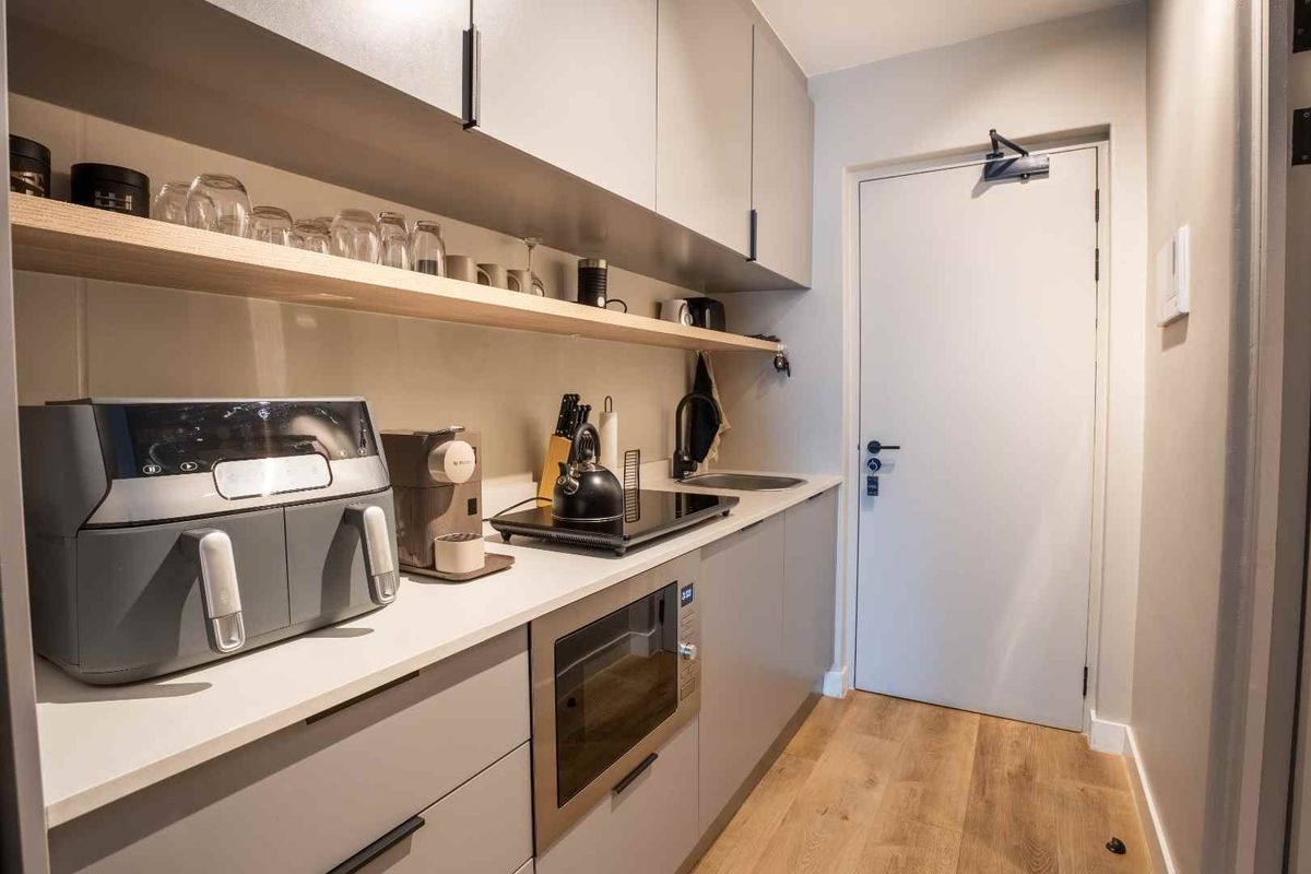 Modern compact kitchen featuring sleek grey cabinetry, stone countertops, integrated microwave, induction hob, and stylish timber shelving with wood-look laminate flooring.