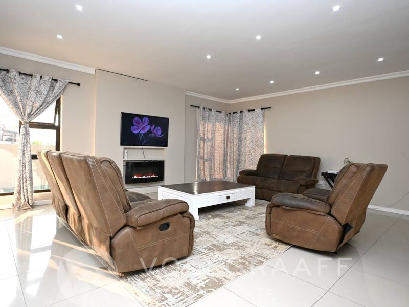 A well-maintained living room featuring tiled flooring, recessed downlighting, and a modern built-in fireplace, creating a comfortable and inviting space.
