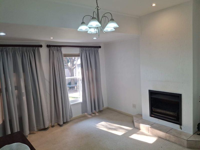 A bright, empty living room featuring a built-in fireplace with a tiled hearth, recessed lighting, and neutral carpeting.