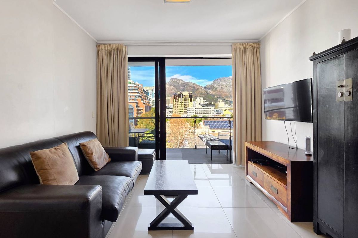 A bright living room featuring large sliding glass doors that open onto a balcony with scenic mountain and city views.