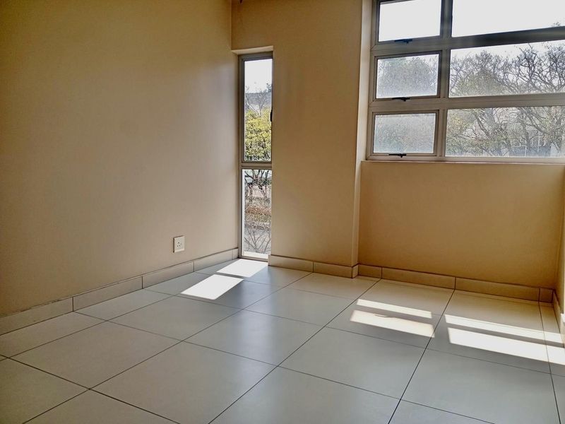 A bright, empty bedroom featuring neutral tiled flooring and large aluminium-framed windows that provide ample natural light.