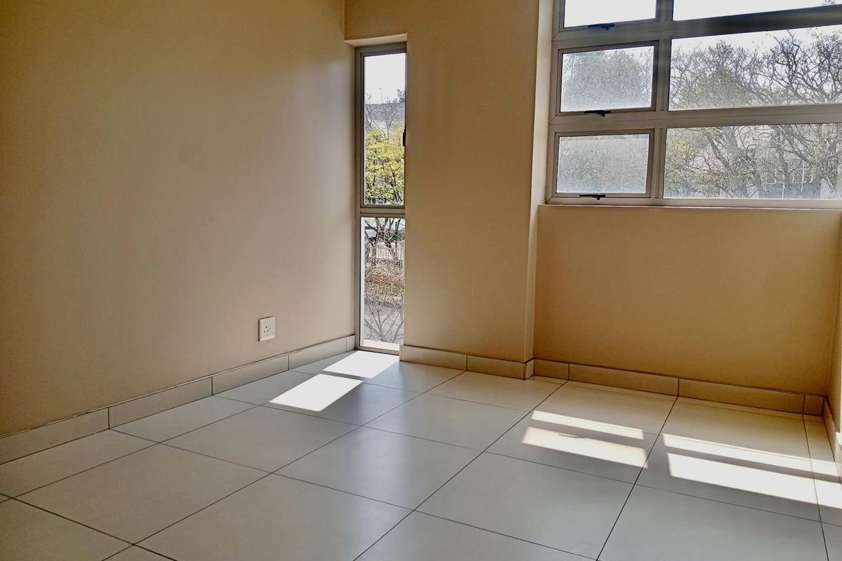 A bright, empty bedroom featuring neutral tiled flooring and large aluminium-framed windows that provide ample natural light.