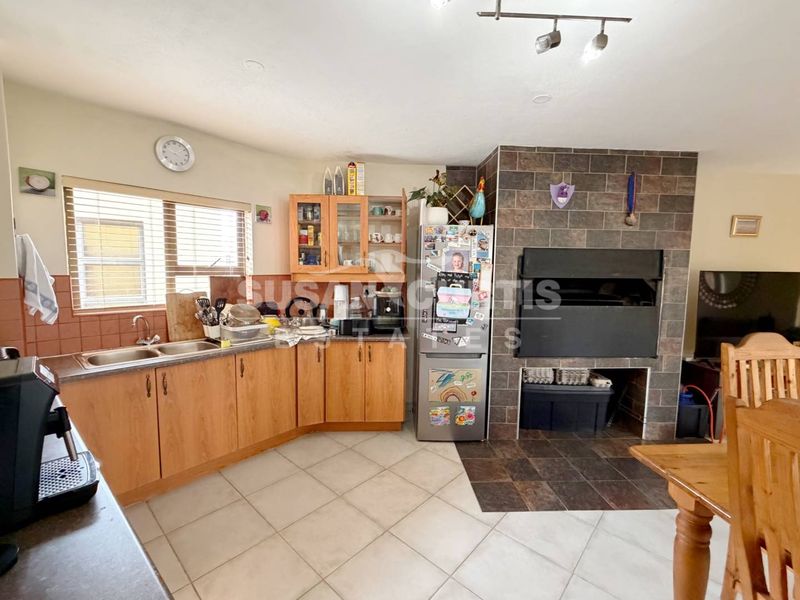 Open-plan kitchen and living area featuring wooden cabinetry, tiled flooring, and a built-in indoor braai with stone-look tiling.
