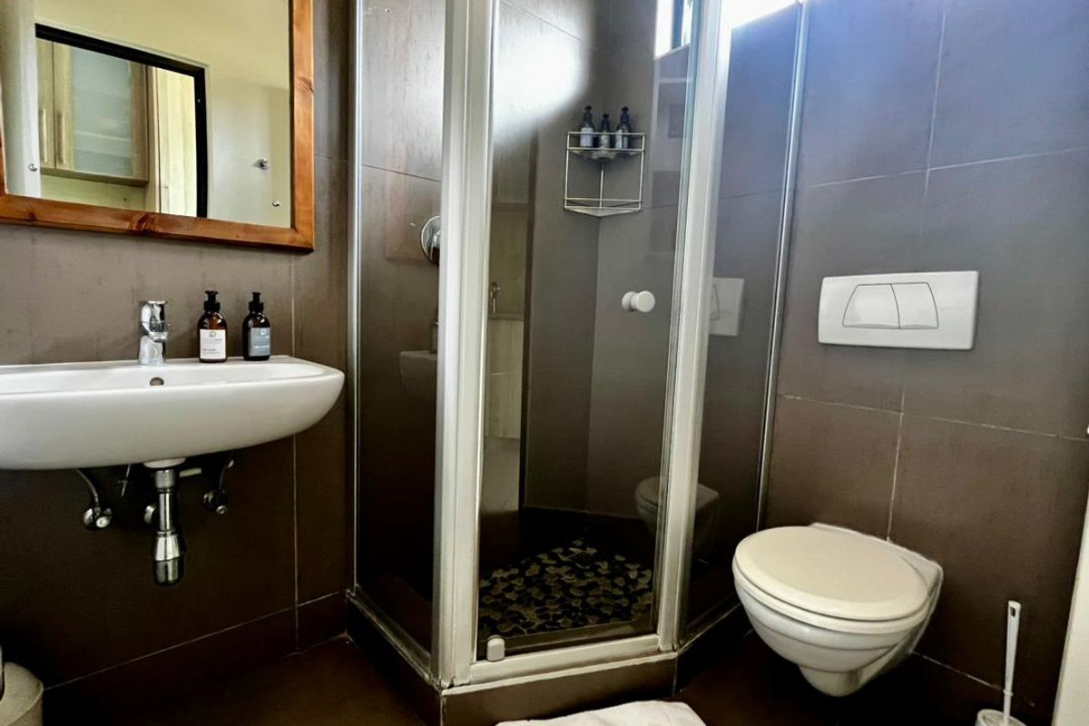 A compact bathroom featuring a wall-mounted basin, a corner shower enclosure, and a wall-hung toilet with a concealed cistern, finished with dark wall tiles.