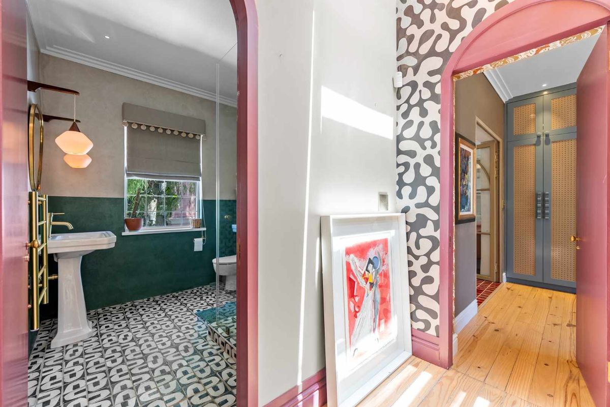 A stylish bathroom featuring a pedestal sink, heated towel rail, and bold patterned floor tiles, connected to a hallway with built-in storage cabinetry.