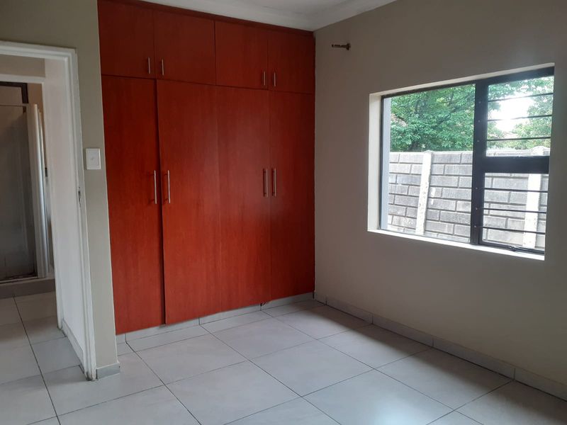 A clean, empty bedroom featuring neutral tiled flooring and ample built-in wooden cupboards, offering a bright and functional space.