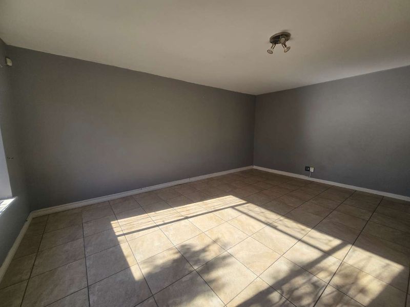 A spacious, empty living area featuring neutral grey walls and durable tiled flooring, providing a blank canvas for interior design.