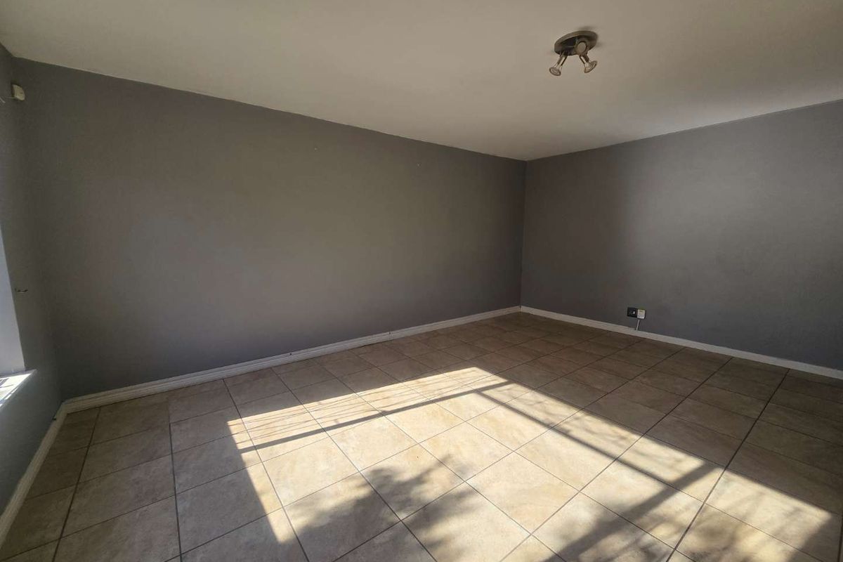 A spacious, empty living area featuring neutral grey walls and durable tiled flooring, providing a blank canvas for interior design.