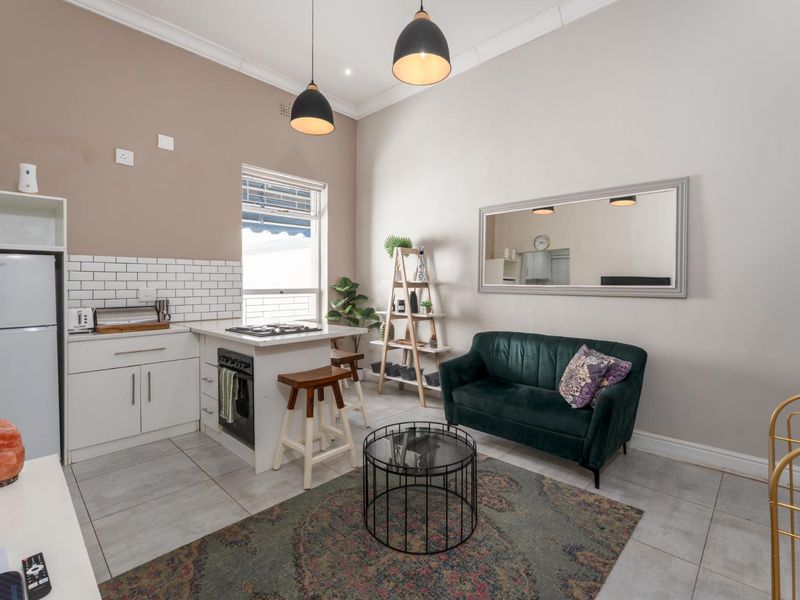 Compact open-plan living area featuring a modern kitchen with subway tile backsplash, built-in oven, gas hob, and neutral ceramic floor tiles.