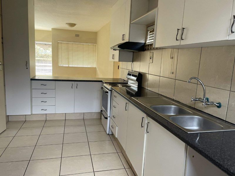 A functional kitchen featuring white cabinetry, a double basin sink, tiled backsplash, and tiled flooring, offering a clean canvas for potential modern updates.