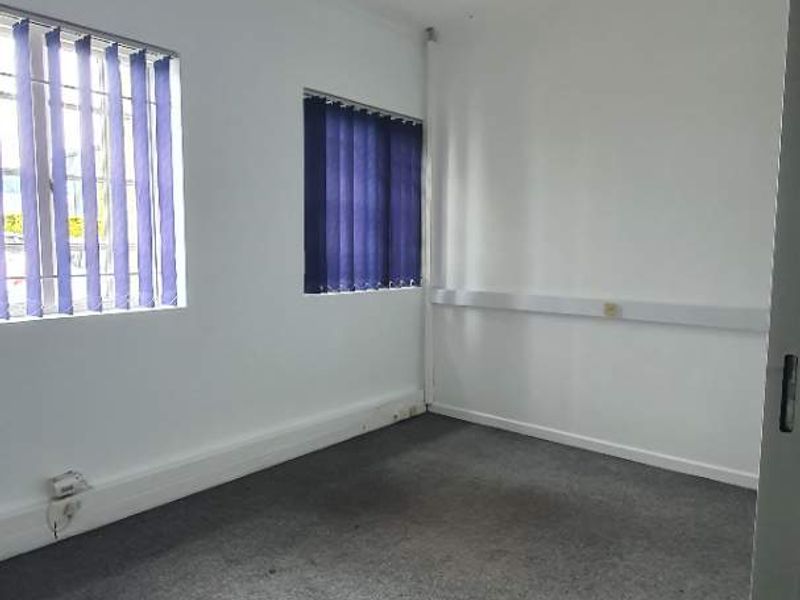 A vacant office space featuring grey carpet flooring, vertical window blinds, and surface-mounted electrical trunking, providing a functional and neutral workspace environment.