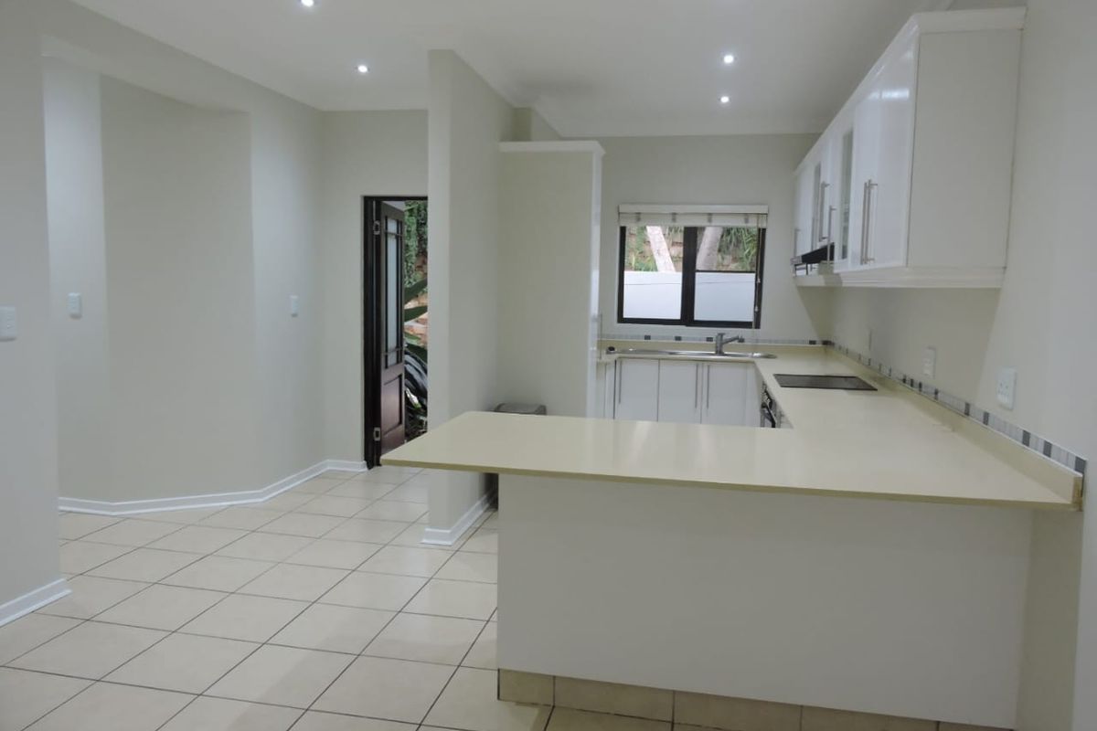 A clean, empty kitchen featuring white cabinetry, light-toned countertops, an electric hob, and tiled flooring with recessed lighting.
