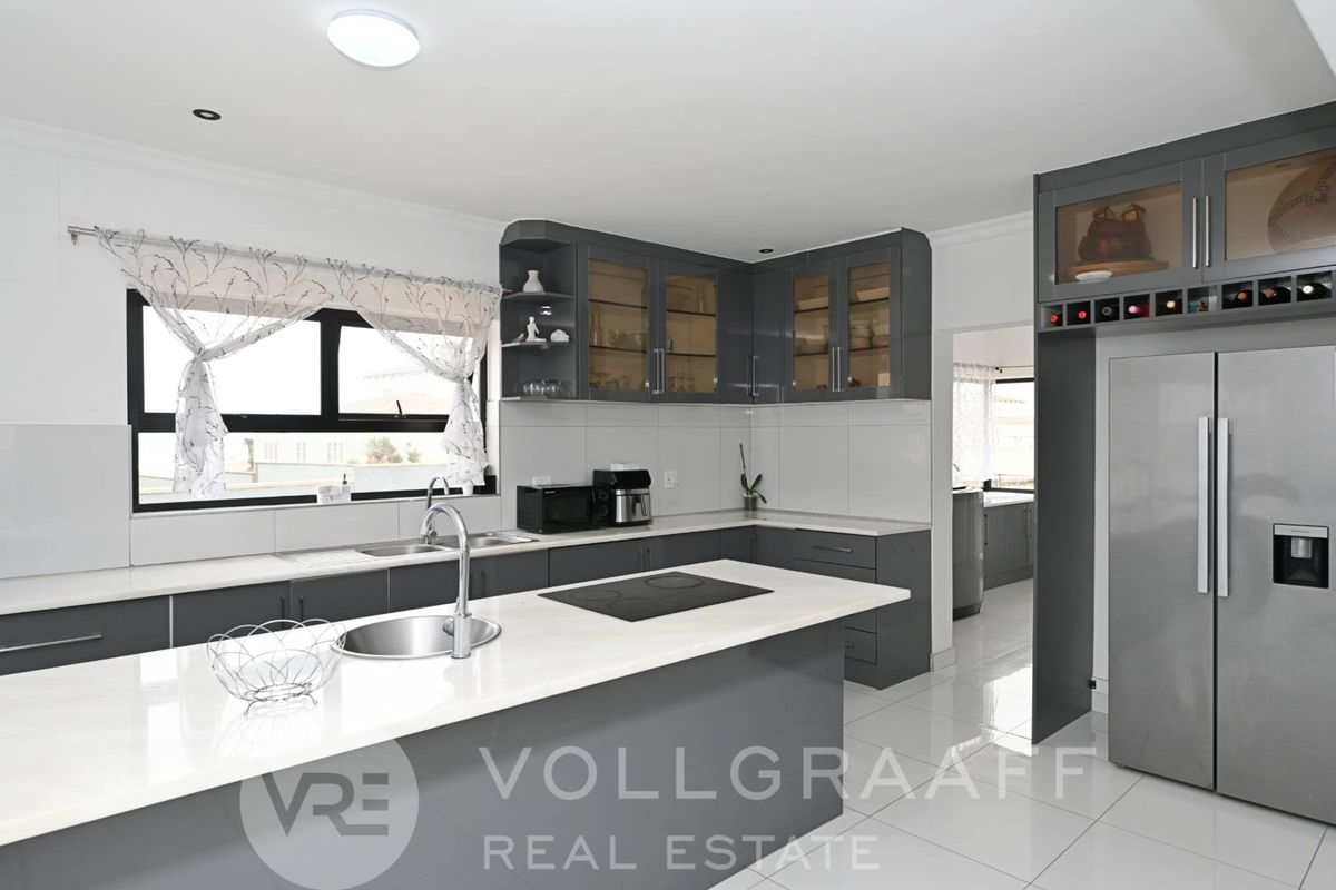 Modern kitchen featuring dark grey cabinetry, white stone countertops, a central island with a built-in hob, and a dedicated scullery area.